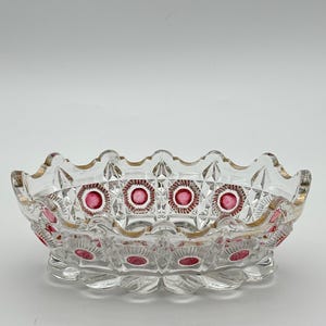 May include: A clear glass bowl with a scalloped rim and a gold-toned edge. The exterior features a geometric diamond-cut pattern interspersed with circular indentations filled with a deep pink colour, creating a decorative and textured appearance.