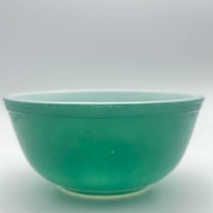 May include: A solid jade green mixing bowl with a smooth, rounded exterior and a wide, open top. The bowl features a slightly lighter interior rim and a consistent, opaque finish throughout the curved body, resting on a circular base.