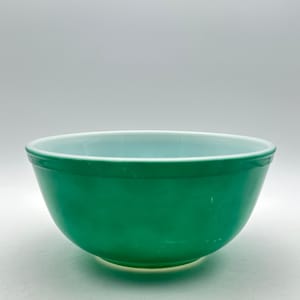 May include: A round mixing bowl made of opaque glass with a smooth, glossy finish. The exterior of the bowl is a vibrant, solid emerald green colour, while the interior features a lighter, pale mint green hue with a wide, circular rim.