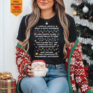 May include: A black short-sleeved t-shirt featuring white text that reads: MONICA, MONICA, HAVE A HAPPY HANUKKAH, SAW SANTA CLAUS, HE SAID HELLO TO ROSS, AND PLEASE TELL JOEY, CHRISTMAS WILL BE SNOWAAAAAAAY, AND RACHEL AND CHANDLER, HASAHERER ANDLERRR.
