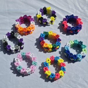 May include: Seven circular bracelets crafted from small, multi-colored plastic beads arranged in a flower-like pattern. Each bracelet features a unique color combination, including shades of pink, blue, yellow, purple, orange, black, and white.