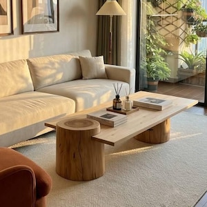 May include: A living room featuring a beige sofa with two matching throw pillows, a rust-coloured armchair, and a rectangular wooden coffee table supported by two thick log-style bases. Two framed abstract prints hang on the wall above the sofa.