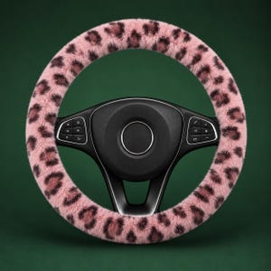 May include: A steering wheel cover featuring a soft, fuzzy texture with a pink and dark brown leopard print pattern. The cover is fitted over a black steering wheel that includes integrated control buttons on the left and right side spokes.