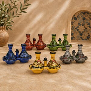 May include: A collection of five double-chambered ceramic condiment servers, each featuring a conical lid and a central handle. The set includes vibrant colour variations in blue, red, green, yellow, and grey, all decorated with intricate floral patterns.