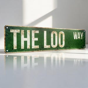 May include: A rectangular green metal sign with a distressed finish and a gold-colored border. The sign features the white text THE LOO WAY in a bold, sans-serif font. There are small circular holes at each of the four corners for mounting.