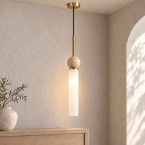 May include: A pendant light fixture featuring a cylindrical frosted glass shade suspended by a thin black cord. The fixture includes a brushed brass canopy, a vertical brass rod, and a spherical beige travertine stone accent above the glass.