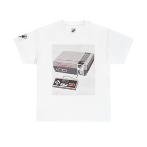 Könnte beinhalten: Ein weißes T-Shirt mit kurzen Ärmeln und einem Grafikdruck einer grauen 8-Bit-Entertainment-System-Konsole sowie einem passenden Controller, die durch ein Kabel verbunden sind. Der Aufdruck enthält den Text 8-BIT ENTERTAINMENT SYSTEM in Rot.