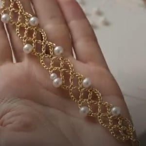 Peut inclure: Un bracelet doré présentant un motif de maillons en treillis délicatement tissé. De petites perles blanches rondes sont intégrées aux intersections des maillons métalliques dorés, créant un design décoratif répétitif sur toute la longueur.