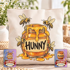 May include: A cream-colored canvas tote bag featuring a graphic illustration of a glass jar overflowing with golden honey. Four yellow and black bees surround the jar, which has the word HUNNY printed in bold black letters on a label.
