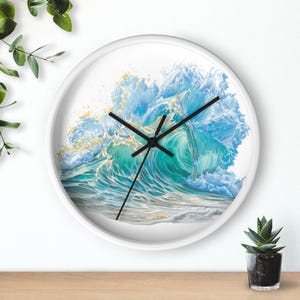 May include: A round wall clock with a white frame and black hands. The clock face features a detailed illustration of a crashing ocean wave in shades of turquoise, light blue, and white, with golden highlights throughout the water spray.