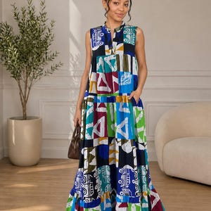 May include: A sleeveless maxi dress featuring a tiered skirt and a vibrant, multi-colored geometric print in shades of blue, green, yellow, and maroon on a black background. The dress has a split neckline and side pockets in a loose silhouette.