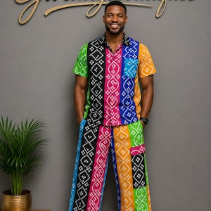 Puede incluir: Una camisa de manga corta con botones y pantalones anchos a juego con un vibrante patrón geométrico multicolor con rayas verticales en verde, negro, rosa, azul y naranja. El conjunto incluye un bolsillo en el pecho y bolsillos laterales.