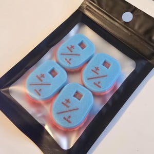 May include: A set of three light blue, oval-shaped foam sponges with a pink base layer, each featuring a small square cutout and a red printed symbol consisting of a plus-minus sign over a division sign, packaged in a black plastic pouch.
