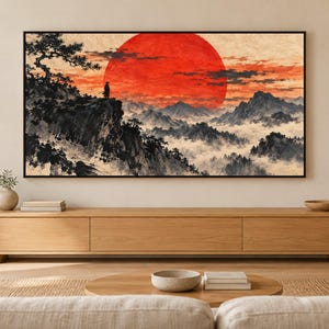 May include: A rectangular wall art print featuring a landscape with a large red sun, a lone figure standing on a rocky cliff, and misty mountains. The artwork uses a black, white, and red color palette with ink-wash style brush strokes.