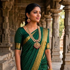 May include: A dark green saree featuring a gold grid pattern and a wide gold border. The garment is paired with a long gold necklace with red and white accents, matching gold drop earrings, and a gold bangle on the wrist, worn with a matching blouse.