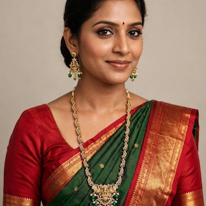 May include: A gold necklace featuring a central pendant with a deity figure, small white stones, and green beads, paired with matching gold drop earrings. The jewelry is worn with a dark green saree featuring a wide red and gold border.