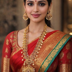 May include: A red and green sari with gold floral embroidery, paired with a long gold necklace featuring red stones and white pearls, and matching gold drop earrings with red stones and white pearls, worn with a small red bindi on the forehead.