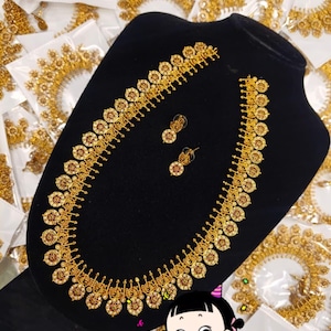 May include: A gold-toned long necklace and matching stud earrings set featuring circular coin-like pendants with intricate embossed detailing and small red and white accents, displayed on a black velvet-covered jewelry bust stand.