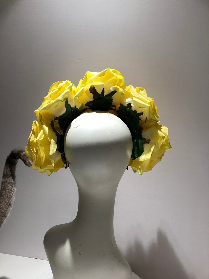 May include: A floral headband featuring a series of large, vibrant yellow artificial roses attached to a dark green base. The roses are arranged in a dense, circular pattern, showcasing layered petals and green foliage accents throughout the design.