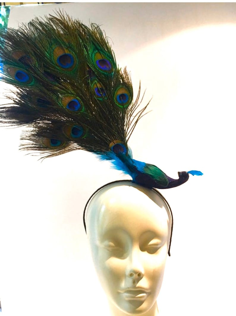 May include: A peacock feather headband with a blue and green peacock design. The headband is black and has a simple design.