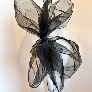 May include: A large black sheer bow with a wired edge. The bow is tied in a knot and is ready to be attached to a hat or other accessory.