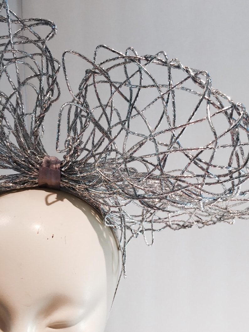 May include: A silver wire headband with a large, intricate bow. The headband is made of thin, interwoven wires that create a delicate and airy look.