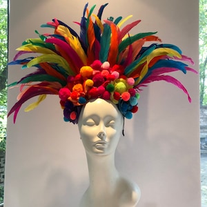 May include: A colorful feather headdress with a band of pom-poms in various colors, including pink, blue, yellow, and green.