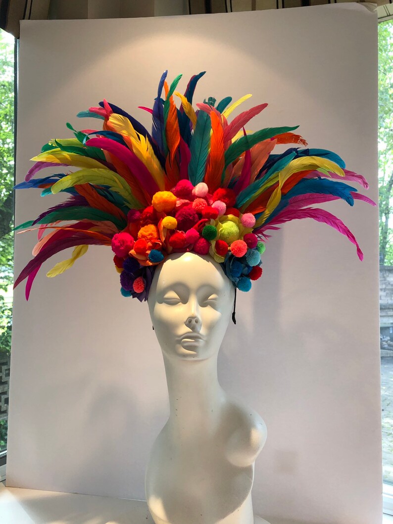 May include: A colorful feather headdress with a band of pom-poms in various colors, including pink, blue, yellow, and green.