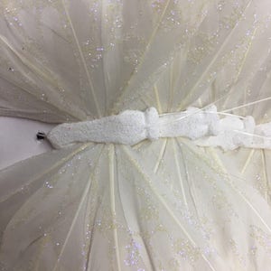 May include: A white butterfly decoration with glitter accents. The butterfly is made of feathers and has a white foam body.