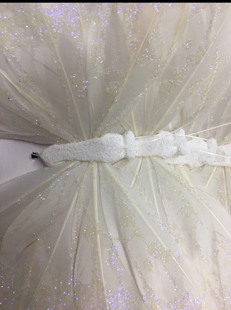 May include: A white butterfly decoration with glitter accents. The butterfly is made of feathers and has a white foam body.