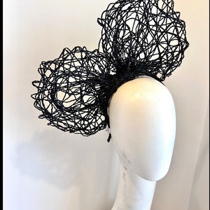 May include: A black, large,  wire mesh headband with two large, rounded,  wire mesh bows. The headband is worn on a white mannequin head.
