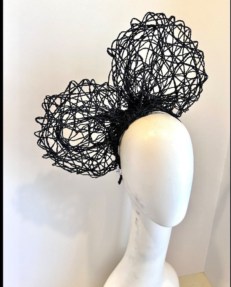May include: A black, large,  wire mesh headband with two large, rounded,  wire mesh bows. The headband is worn on a white mannequin head.