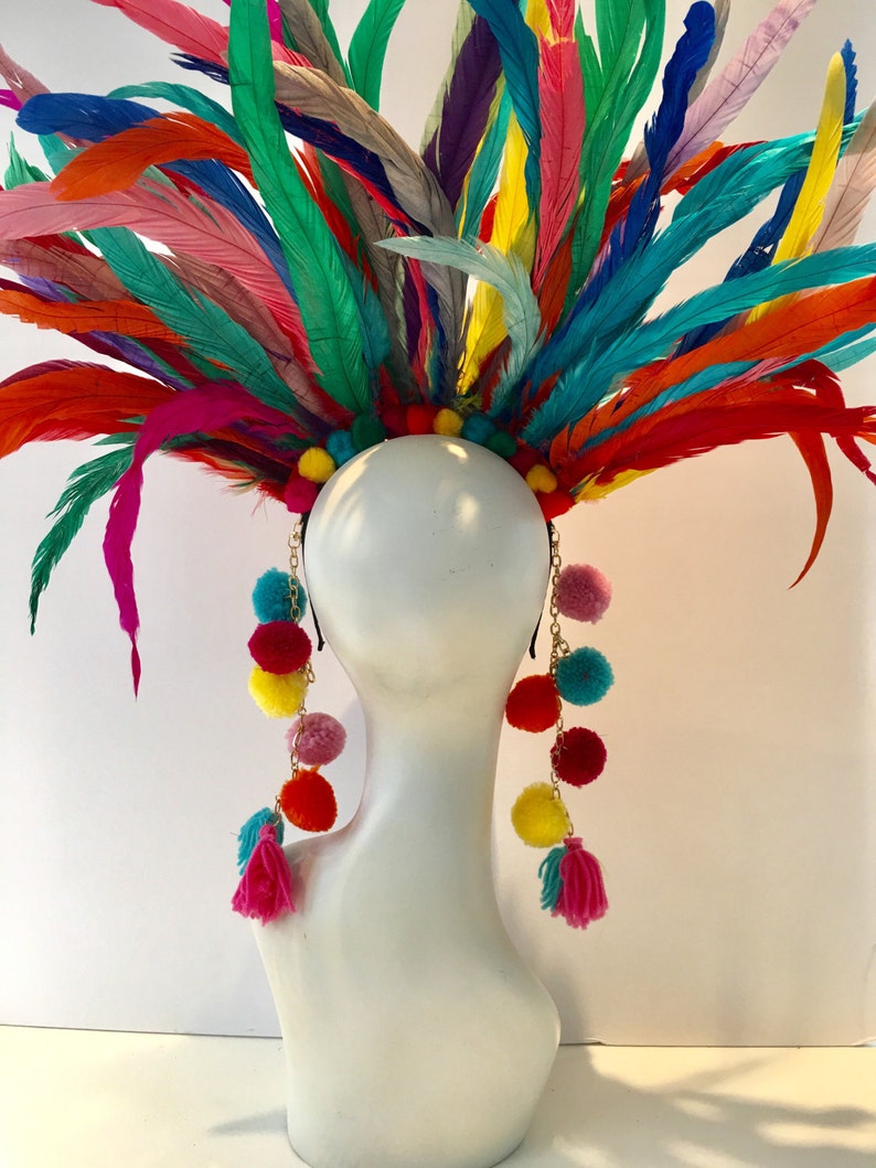 May include: A colorful feather headdress with long strands of pom-poms and tassels hanging down the sides. The headdress is made of a variety of feathers in shades of pink, blue, green, yellow, and orange. The pom-poms are also in a variety of colors, including pink, yellow, red, and blue.