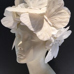 May include: A white headpiece made of paper butterflies and flowers. The headpiece is worn on a white mannequin head.