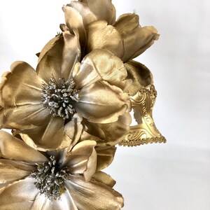 K&ouml;nnte beinhalten: Ein goldfarbener floraler Haarschmuck mit gro&szlig;en, geschichteten Bl&uuml;tenbl&auml;ttern und einem dekorativen Filigranakzent. Die Blumen haben silberfarbene Zentren. Der Haarschmuck ist wahrscheinlich f&uuml;r einen besonderen Anlass oder ein Kost&uuml;m.