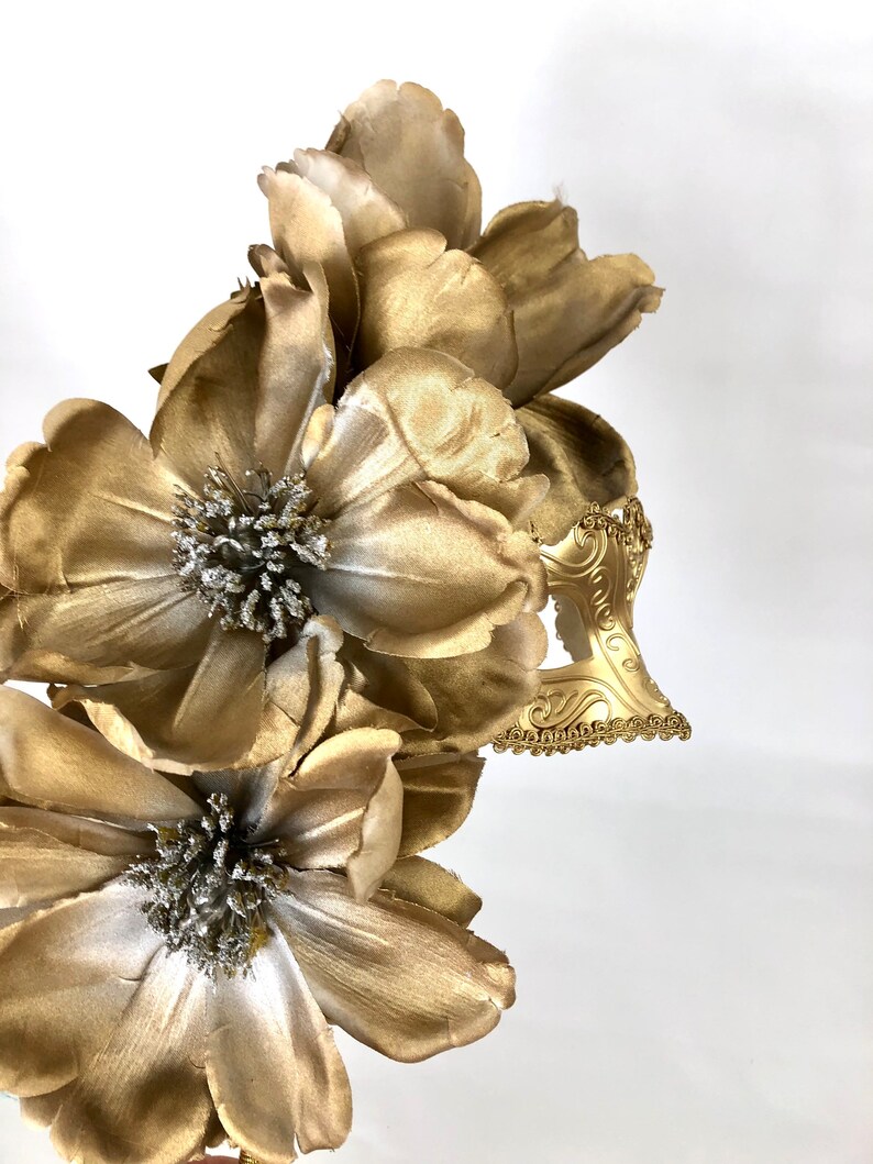 K&ouml;nnte beinhalten: Ein goldfarbener floraler Haarschmuck mit gro&szlig;en, geschichteten Bl&uuml;tenbl&auml;ttern und einem dekorativen Filigranakzent. Die Blumen haben silberfarbene Zentren. Der Haarschmuck ist wahrscheinlich f&uuml;r einen besonderen Anlass oder ein Kost&uuml;m.