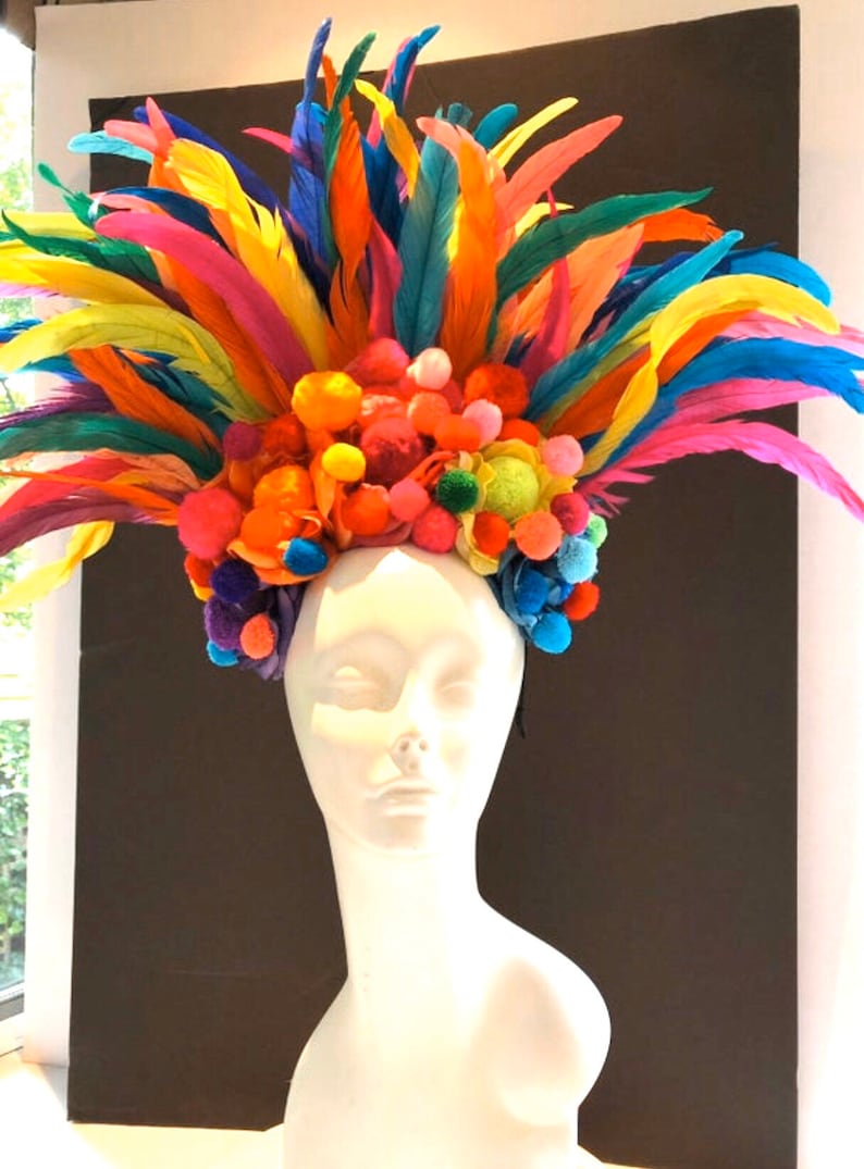 May include: A colorful headpiece with a base of bright orange, pink, and green pom-poms and a crown of rainbow feathers.