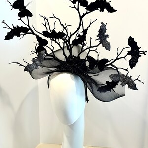 May include: A black Halloween headpiece featuring a tree branch design with bats and butterflies. The headpiece is made of black branches, glittery bats, and butterflies. The base is a black headband with a black mesh accent.