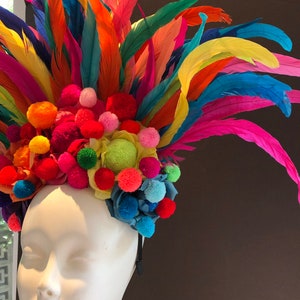 May include: A colorful headband with a rainbow of feathers and pom-poms. The headband is made of a black elastic band and is decorated with a variety of colors, including red, orange, yellow, green, blue, and purple.
