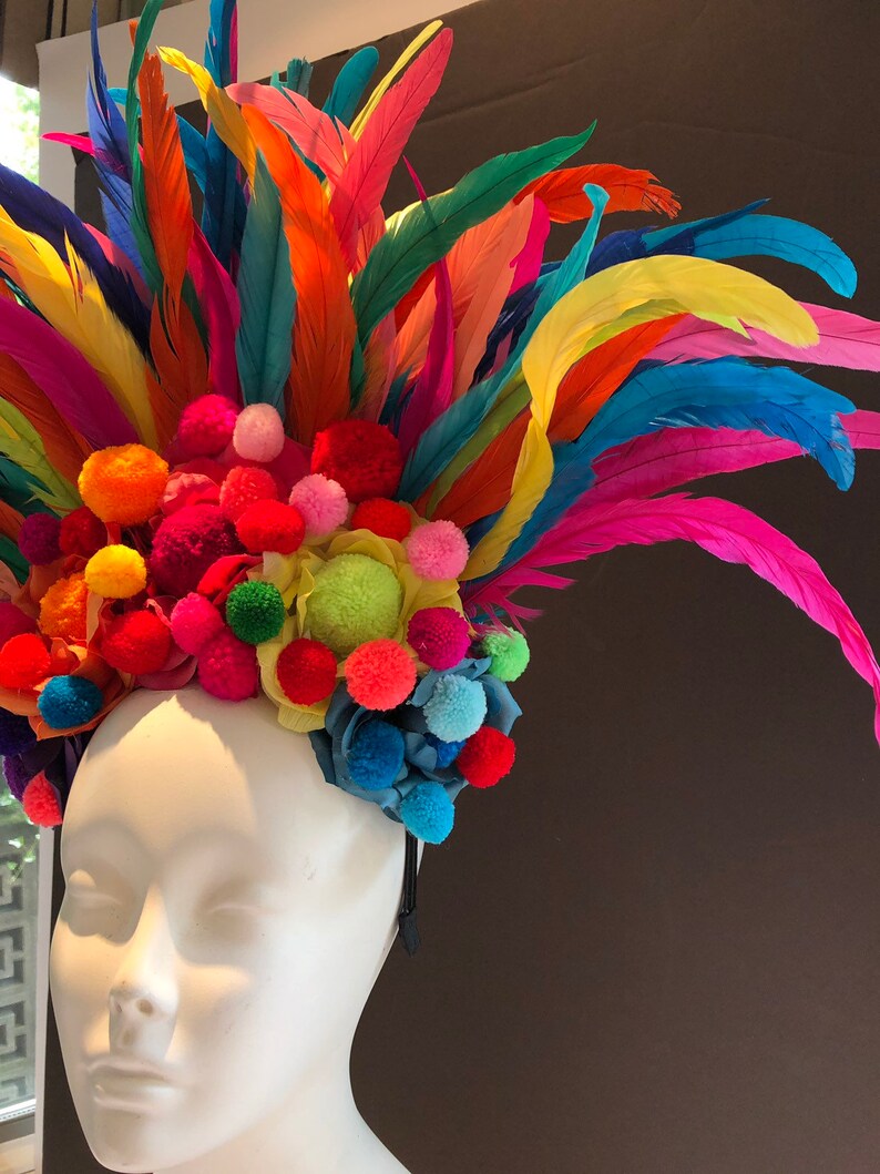 May include: A colorful headband with a rainbow of feathers and pom-poms. The headband is made of a black elastic band and is decorated with a variety of colors, including red, orange, yellow, green, blue, and purple.