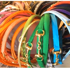 May include: A collection of colorful ribbon headbands with gold horse bit accents. The headbands are arranged in a circular pattern, with the gold accents facing outward.