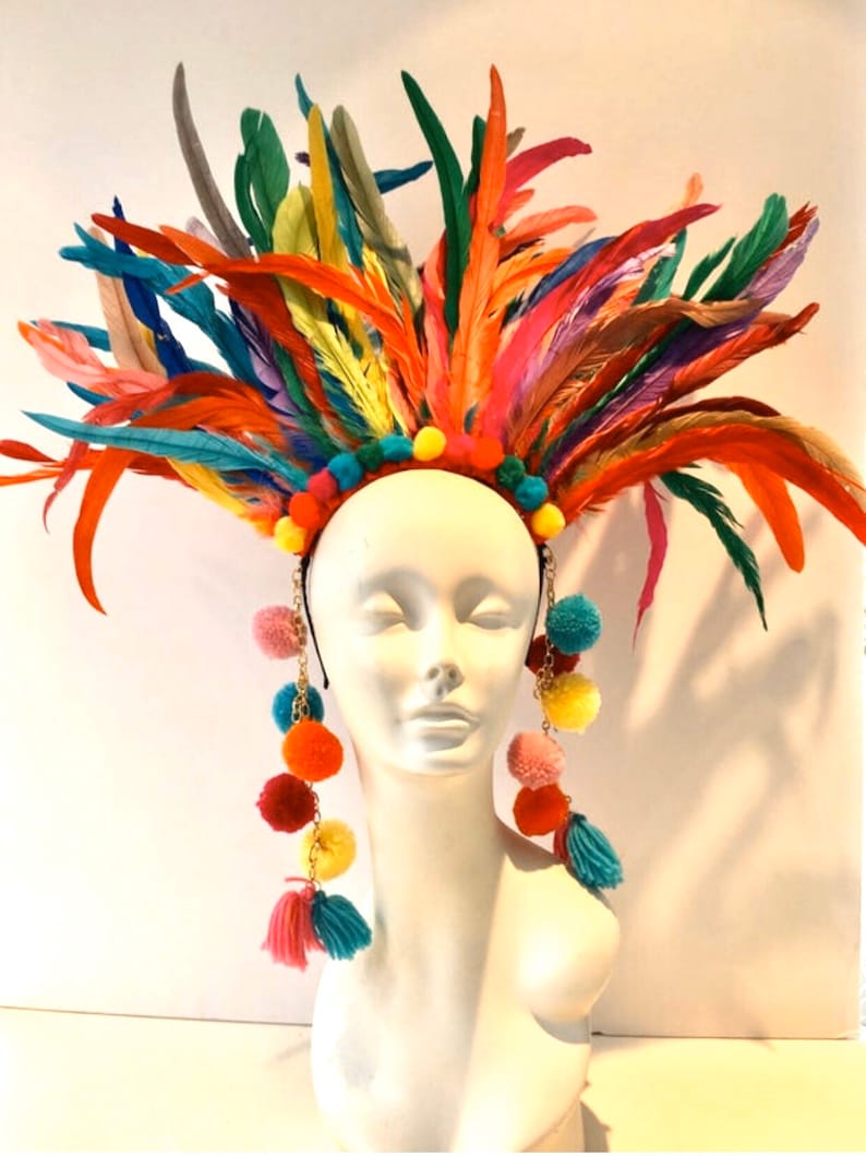 May include: A colorful feather headdress with a headband and dangling pom-poms. The headdress is made of feathers in various colors, including red, orange, yellow, green, blue, and purple. The pom-poms are also in various colors, including red, orange, yellow, green, blue, and pink.
