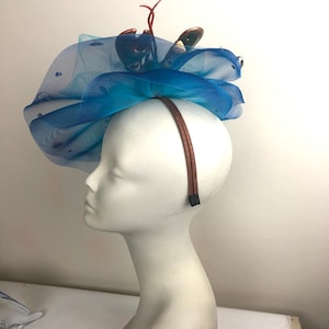 Op de afbeelding: Een blauwe tule hoofdband met een kreeftdecoratie. De hoofdband wordt gedragen op een wit mannequinhoofd.