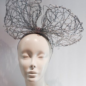 May include: A silver wire mesh headband with a large bow. The headband is worn on a white mannequin head.