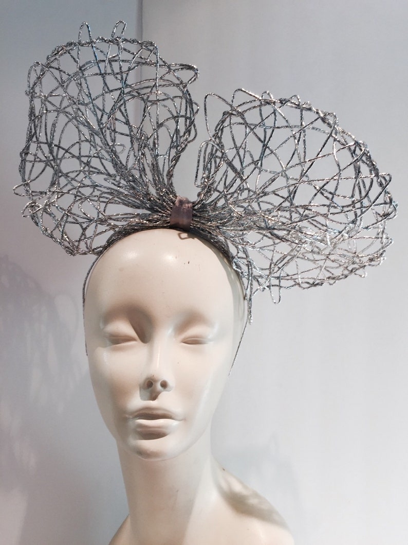 May include: A silver wire mesh headband with a large bow. The headband is worn on a white mannequin head.