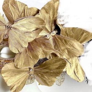 Puede incluir: Una m&aacute;scara dorada con grandes alas de mariposa estilizadas. Las alas est&aacute;n hechas de un material texturizado y est&aacute;n adornadas con peque&ntilde;os adornos brillantes. La m&aacute;scara parece estar dise&ntilde;ada para un disfraz o evento especial.
