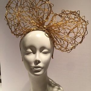 May include: A gold wire headband with two large, overlapping bows. The bows are made of a delicate, interwoven wire mesh.