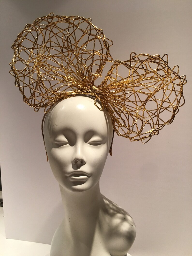 May include: A gold wire headband with two large, overlapping bows. The bows are made of a delicate, interwoven wire mesh.