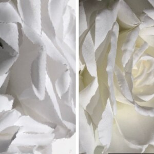 May include: A close-up view of a white artificial rose with layered, delicate petals. The flower features soft, matte-textured edges and a dense, spiraled center, showcasing a clean, monochromatic appearance with subtle shadows between the petals.