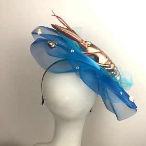 Op de afbeelding: Een blauw tule haarband met een gouden kreeft en witte schelpen. De haarband zit op een wit mannequinhoofd.